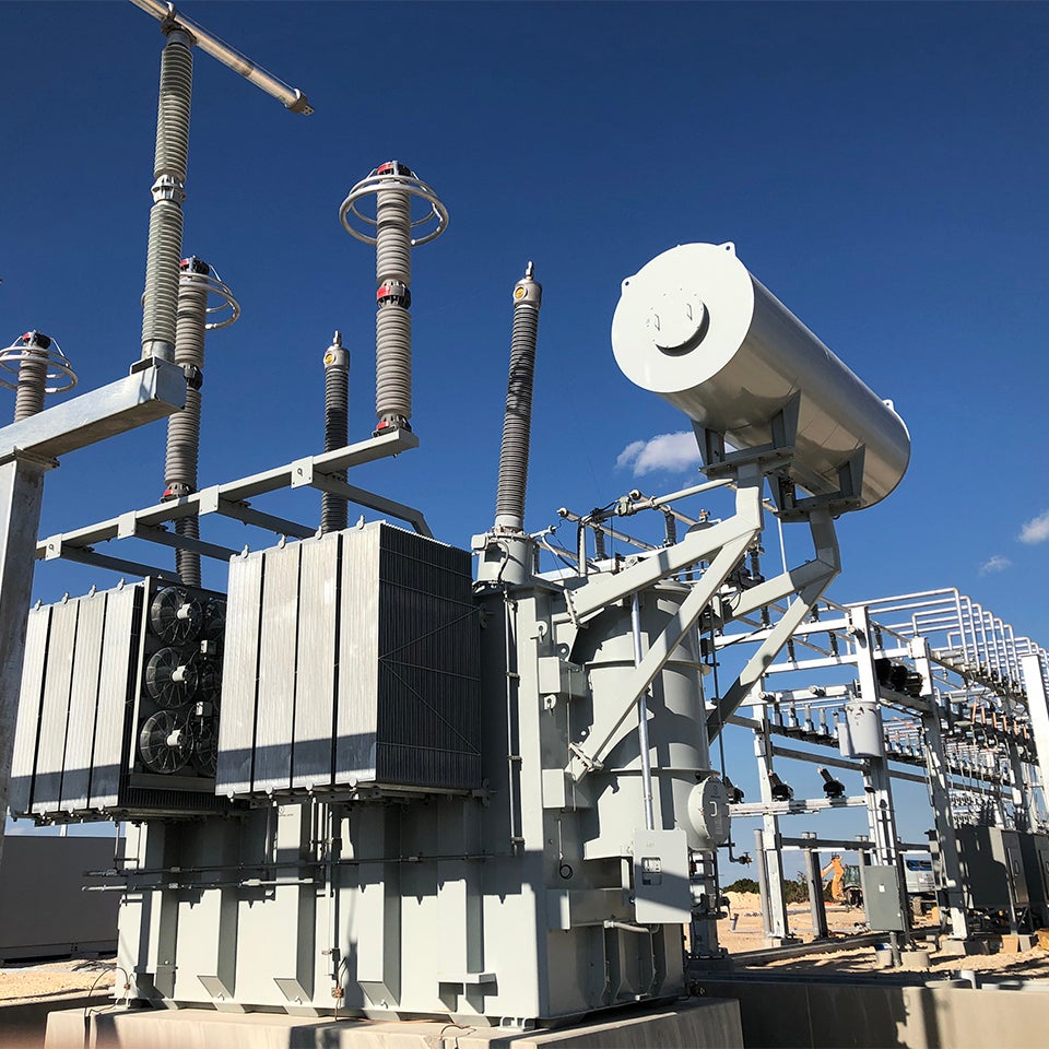 Close-up terminal dan isolator trafo step-up di gardu induk, latar belakang kabut